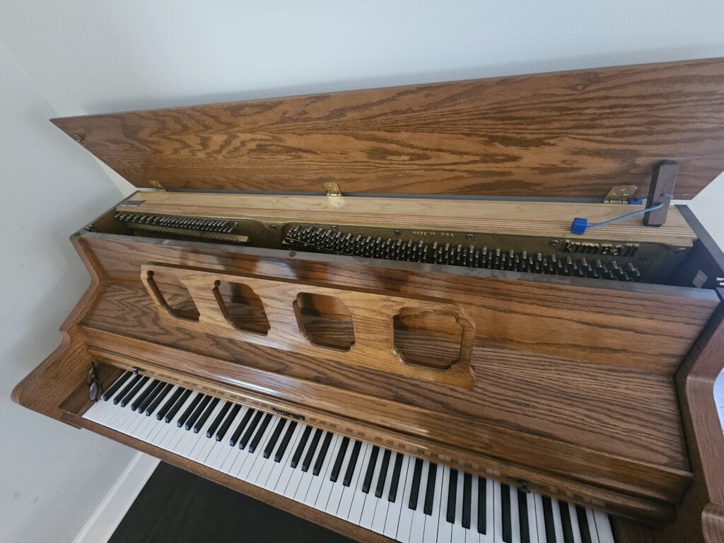 A Kimball studio piano with the lid open, revealing the serial number location.