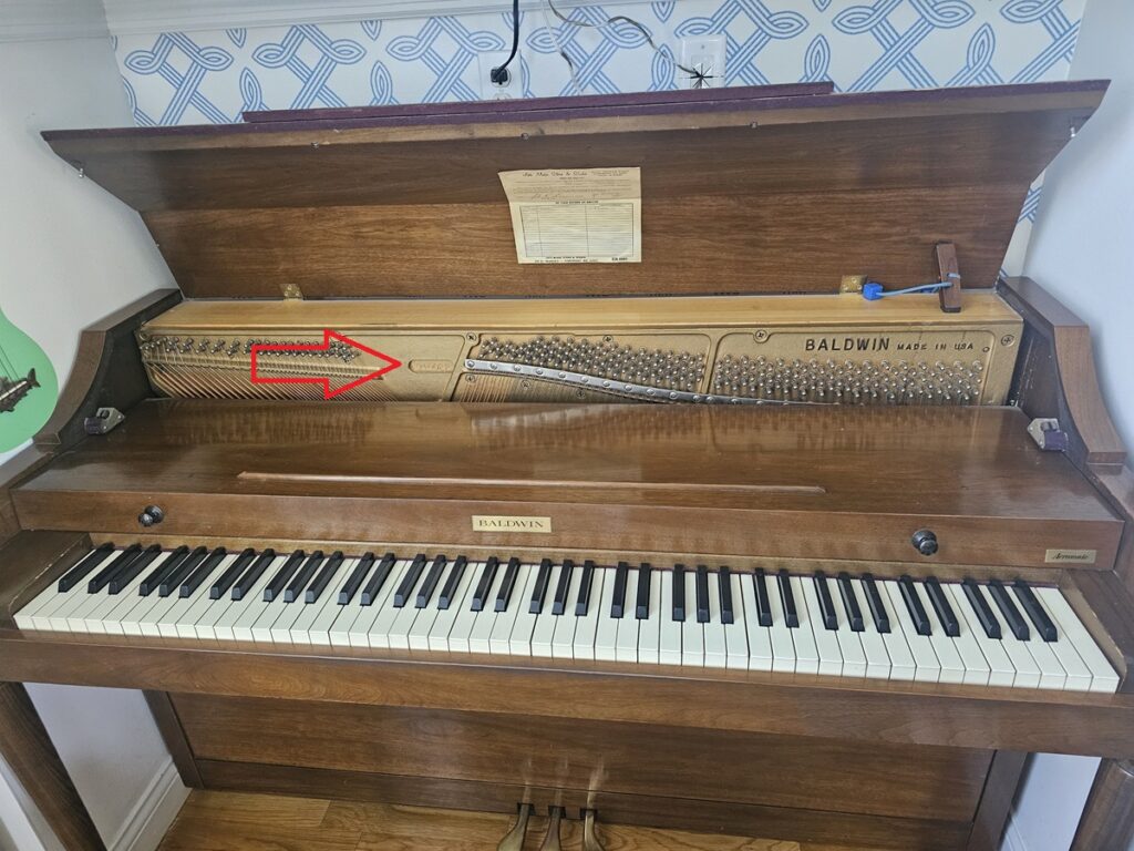 A Baldwin spinet piano with the lid open, revealing the serial number location.