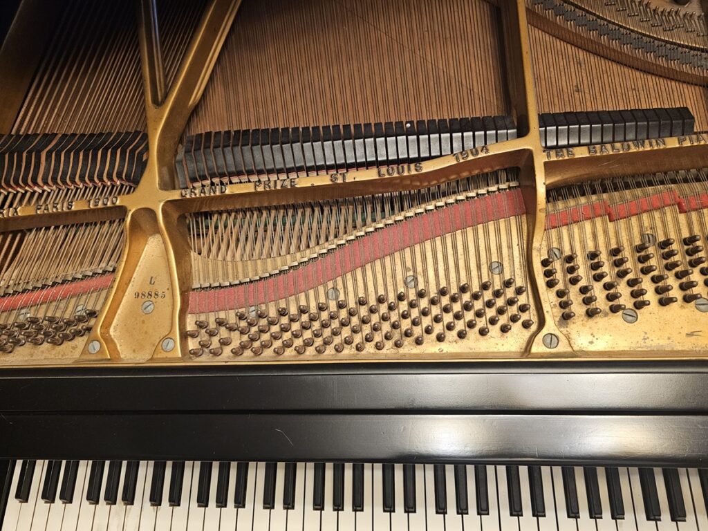 A Baldwin grand piano with the lid open, revealing the serial number location.