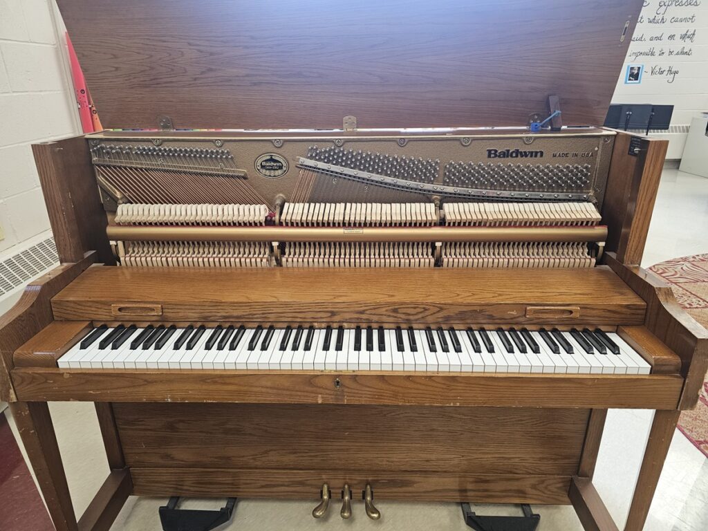 A Baldwin upright piano with the lid open, revealing the serial number location.