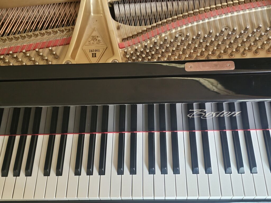 A Boston grand piano with the lid open, revealing the serial number location.