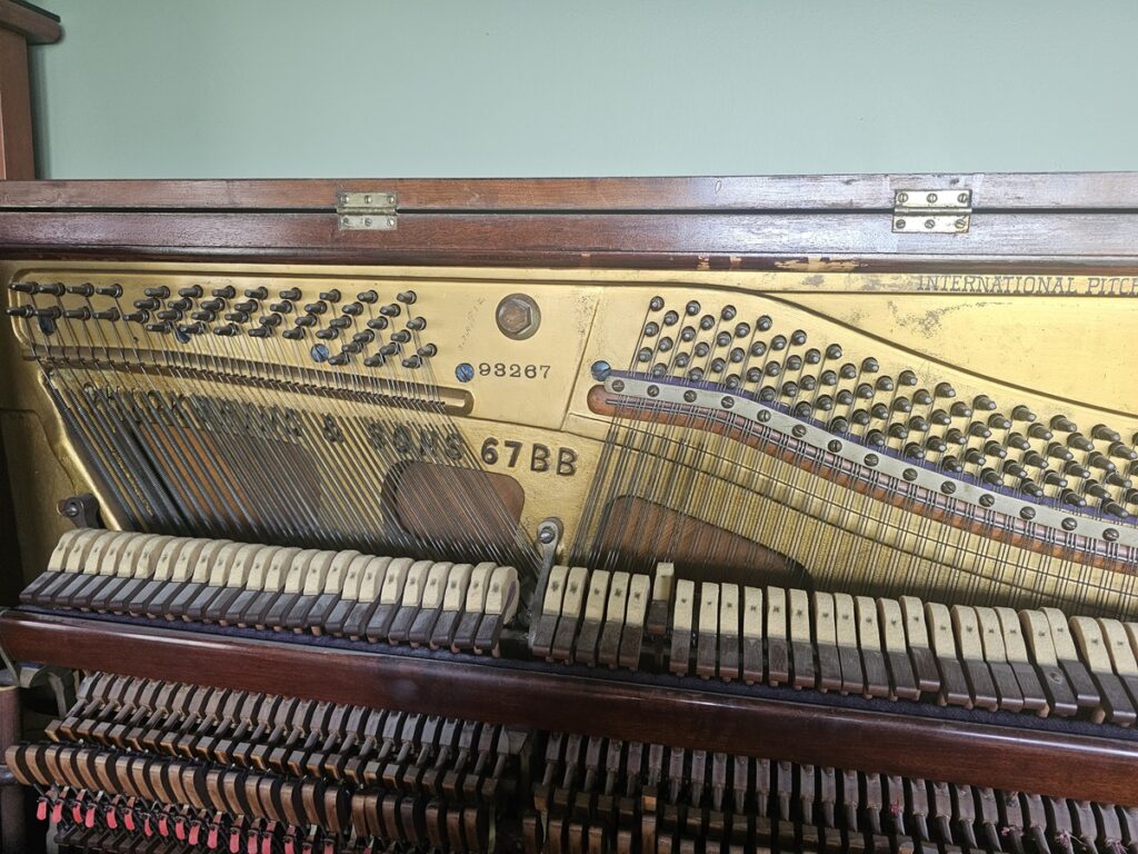 Chickering & Sons upright piano with lid open, showing the location of the serial number.