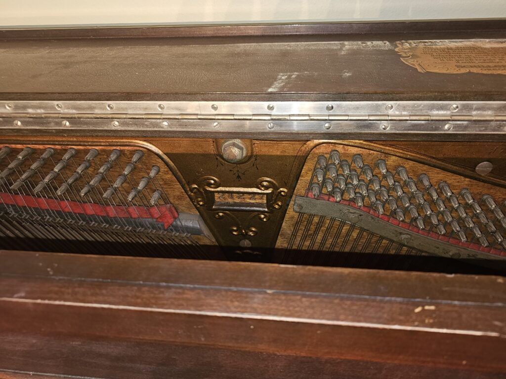A Schiller upright piano with the lid open, revealing the serial number location.