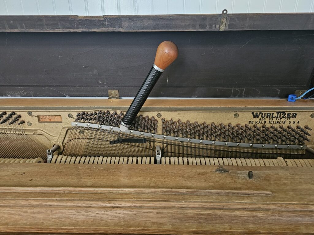 A Wurlitzer spinet piano with the lid open, revealing the serial number location.