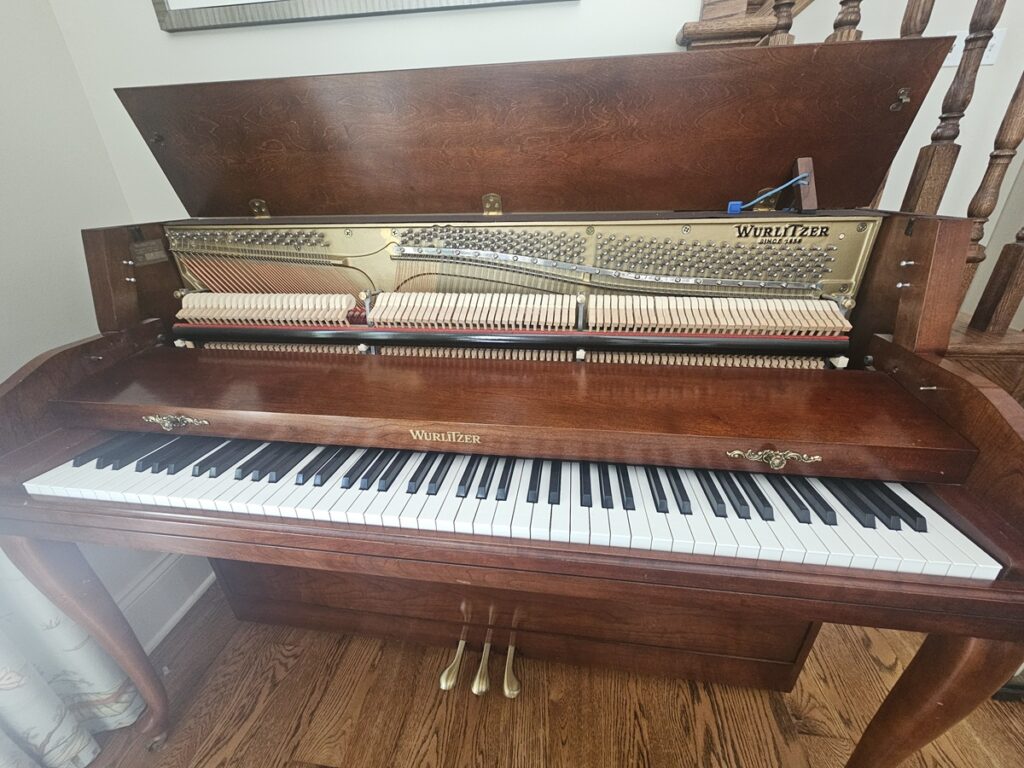 A Wurlitzer studio piano with the lid open, revealing the serial number location.