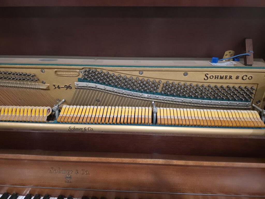 A Sohmer upright piano with the lid open and the front removed.