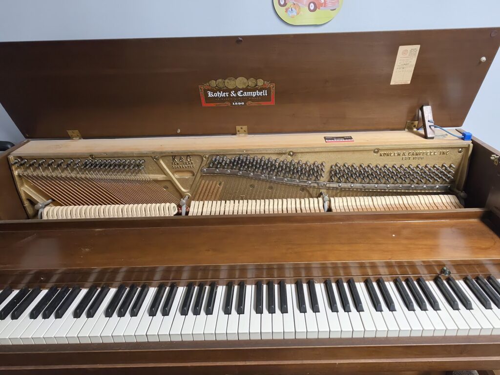 A Kohler & Campbell spinet piano with the lid open and the front removed.