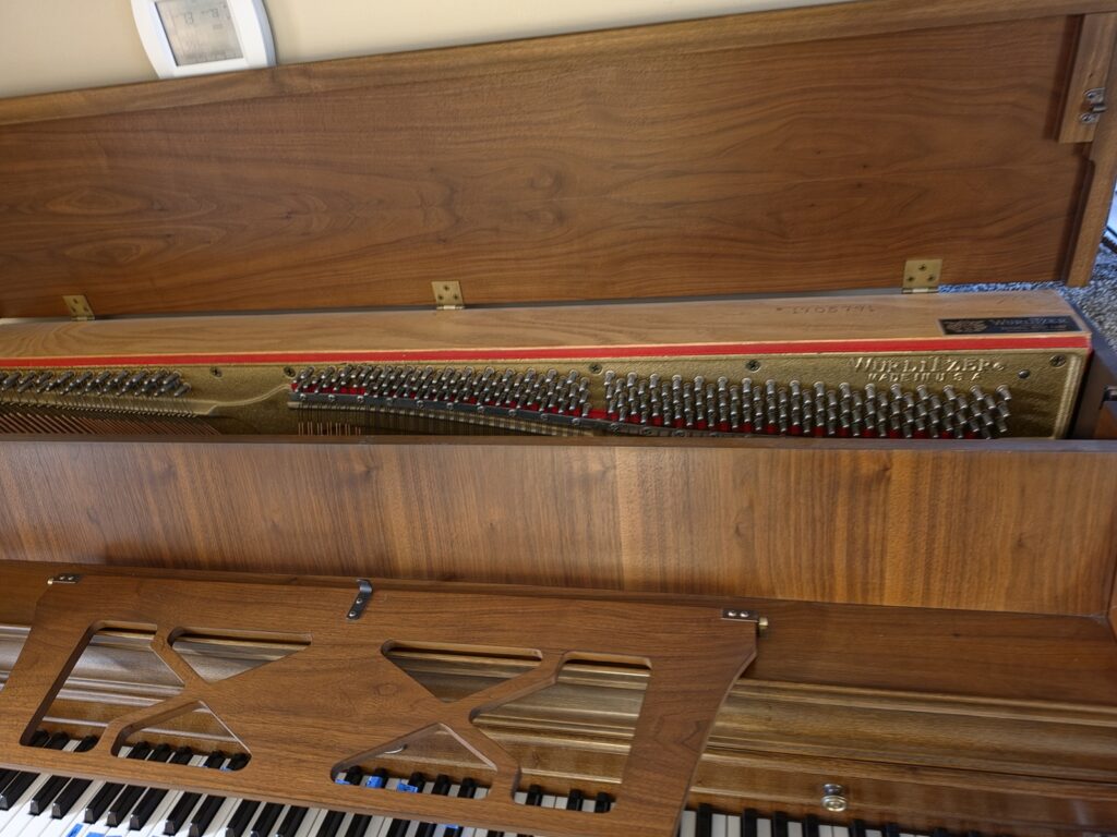 A Wurlitzer console piano with the lid open.